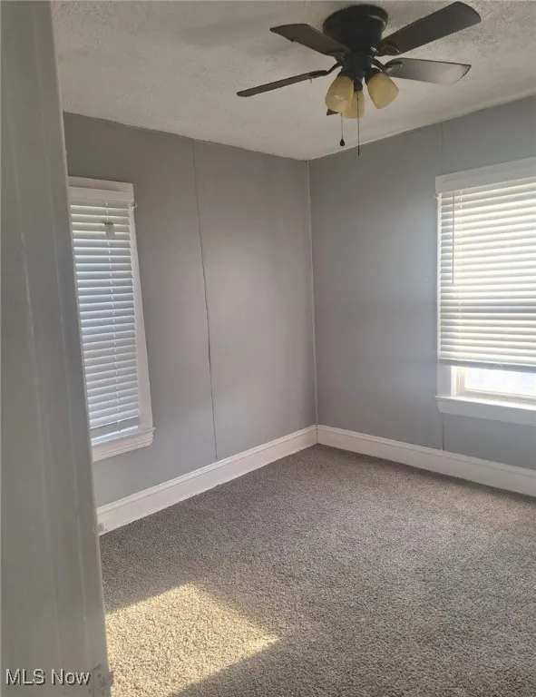 Carpeted empty room featuring a textured ceiling and a ceiling fan