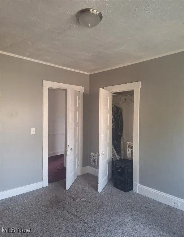 Unfurnished bedroom with carpet, a textured ceiling, and ornamental molding
