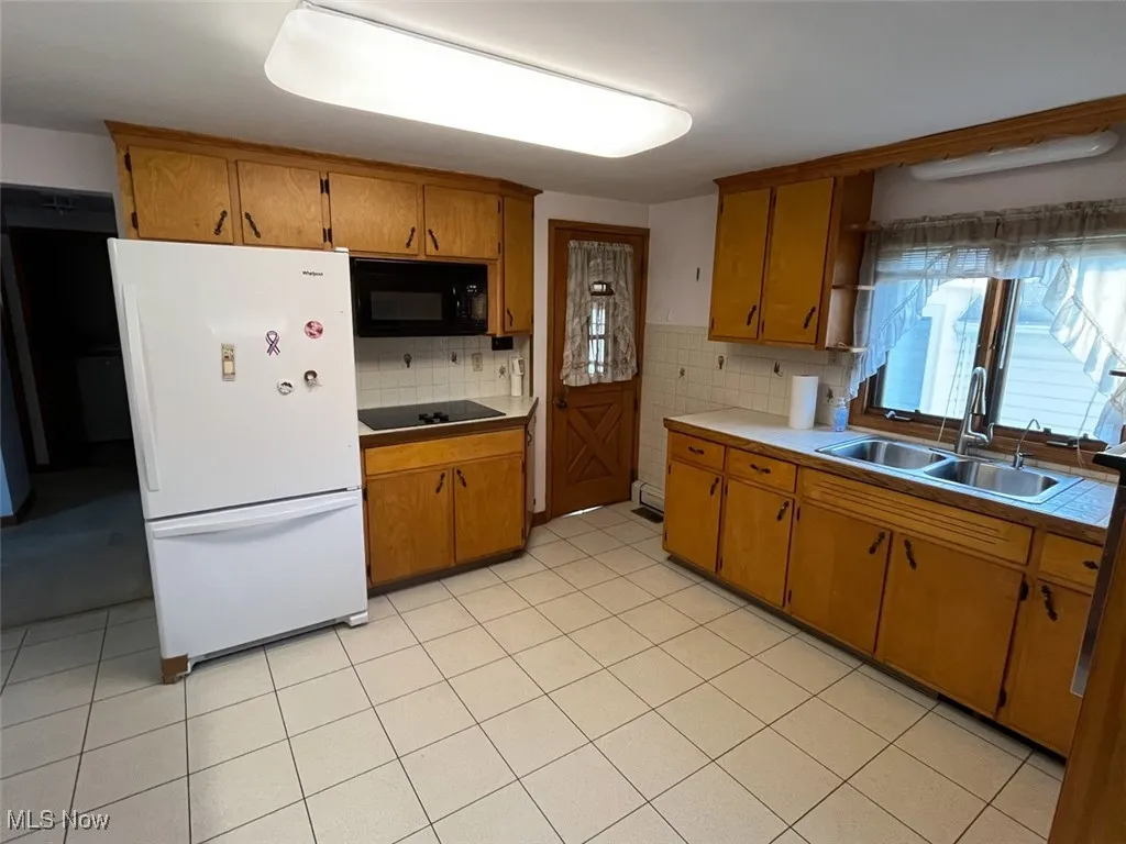 Kitchen with tasteful backsplash, black appliances, brown cabinets, and light tile patterned floors
