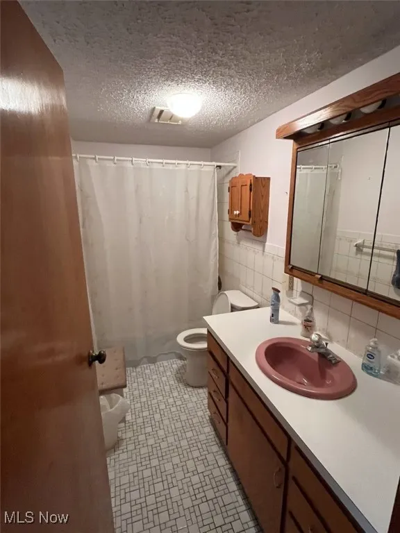 Bathroom featuring vanity, a textured ceiling, tile walls, decorative backsplash, and shower / bathtub combination with curtain
