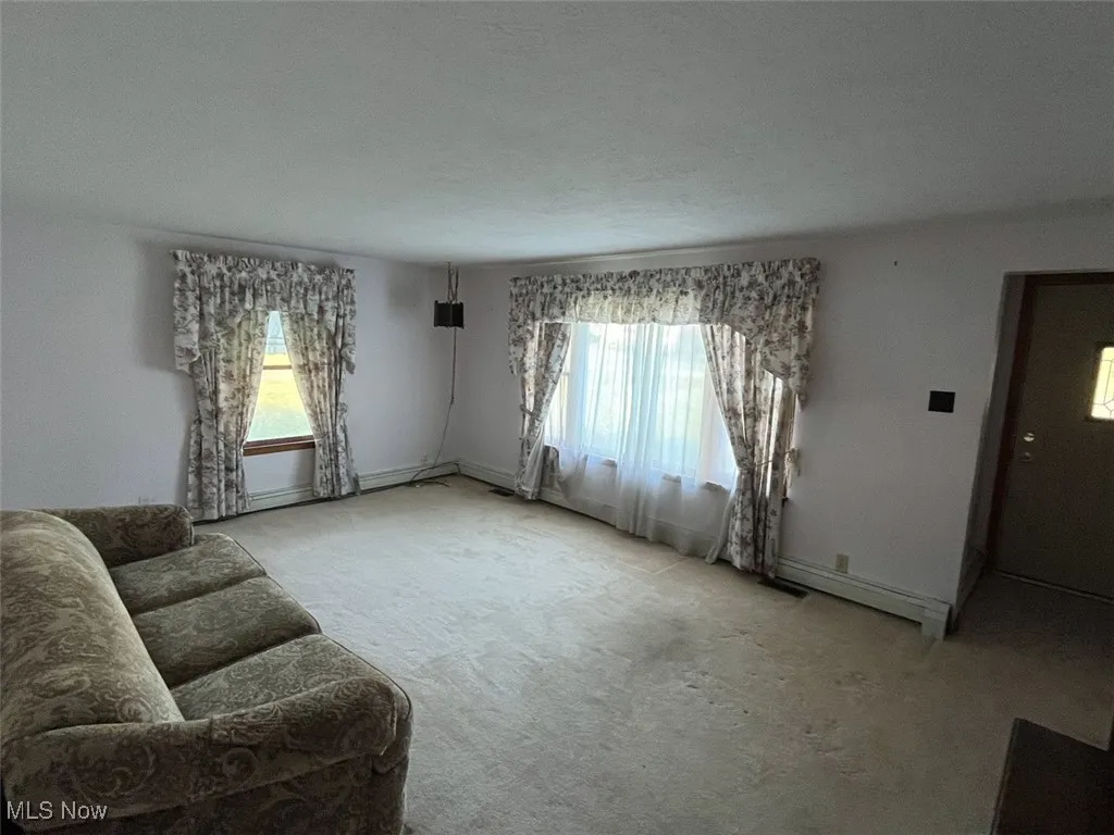 Unfurnished living room with carpet flooring and baseboard heating