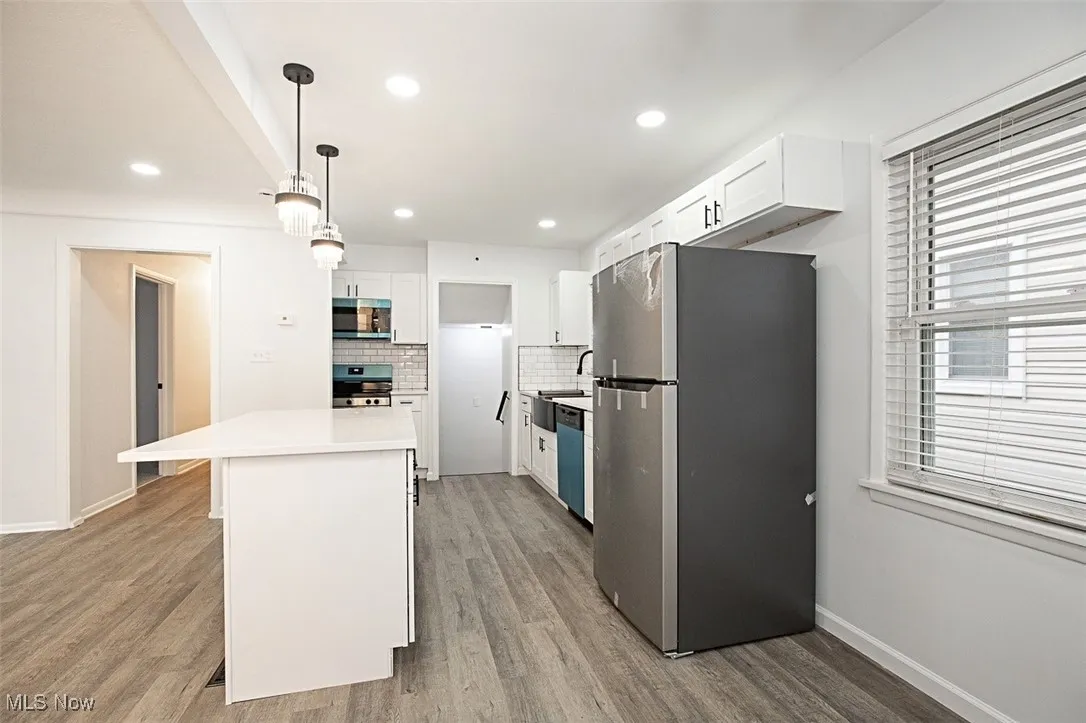 Kitchen featuring white cabinetry, appliances with stainless steel finishes, hanging light fixtures, tasteful backsplash, and light wood-type flooring