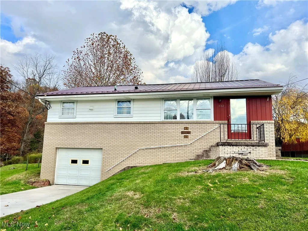 View of front of house featuring brick siding, a front lawn, a garage, and a metal roof