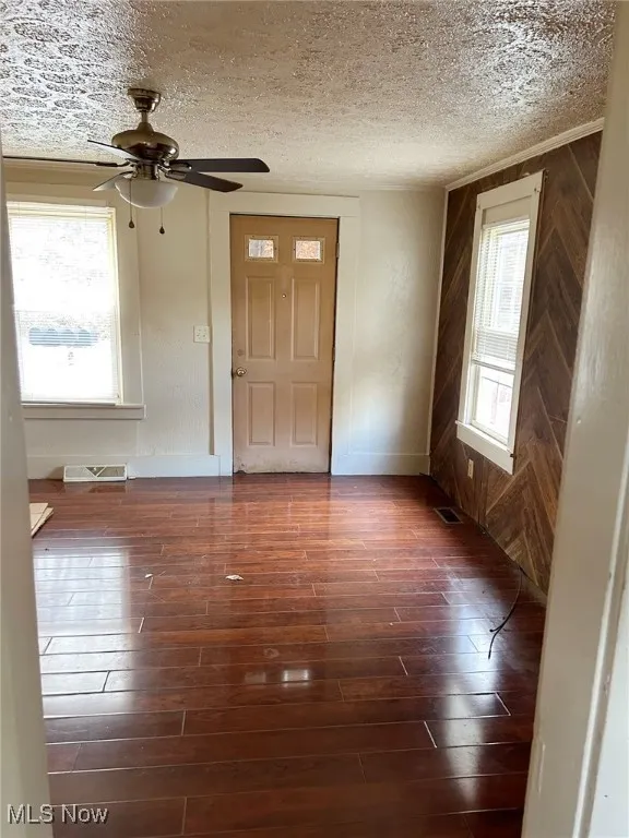 Living room with a textured ceiling, dark wood-style floors, a ceiling fan, and wood walls