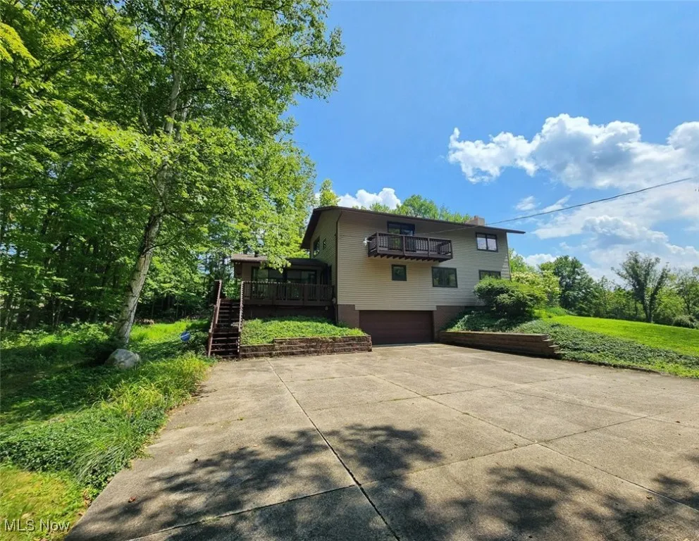 View of side of house with a deck, driveway, a garage, a chimney, and stairway