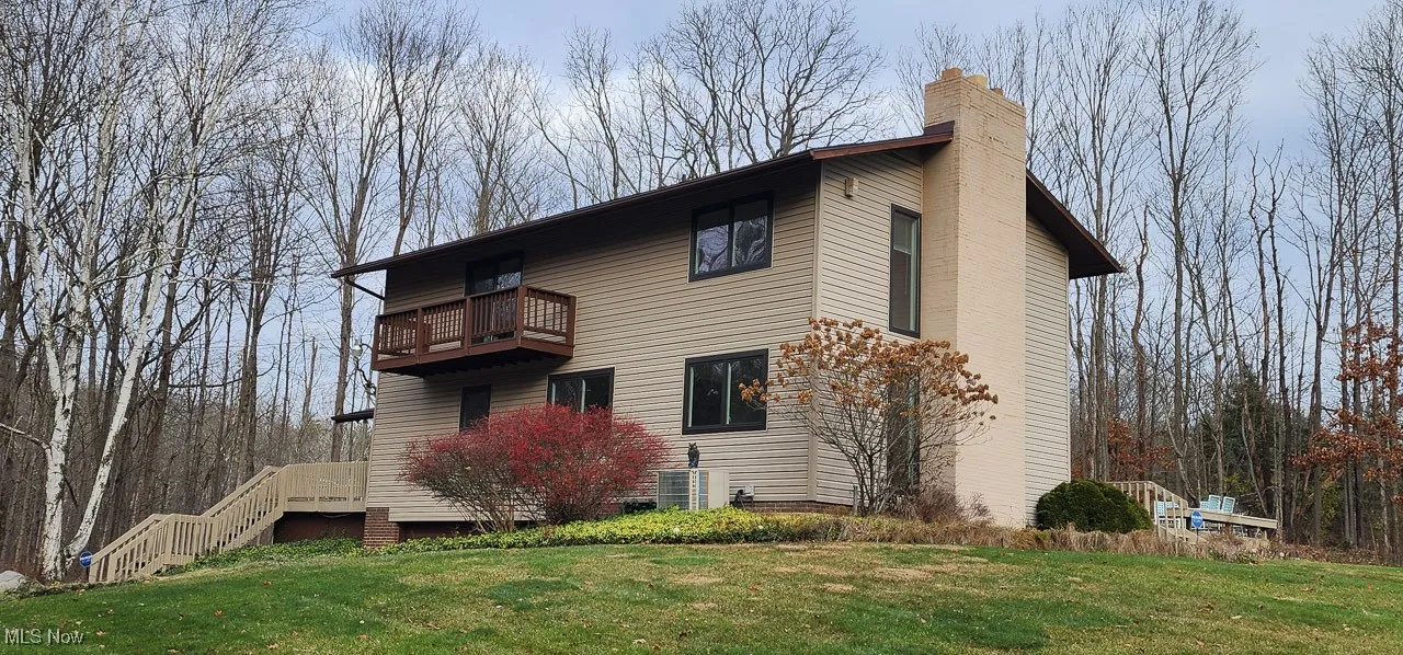 View of home's exterior featuring a balcony, a yard, a chimney, and stairway
