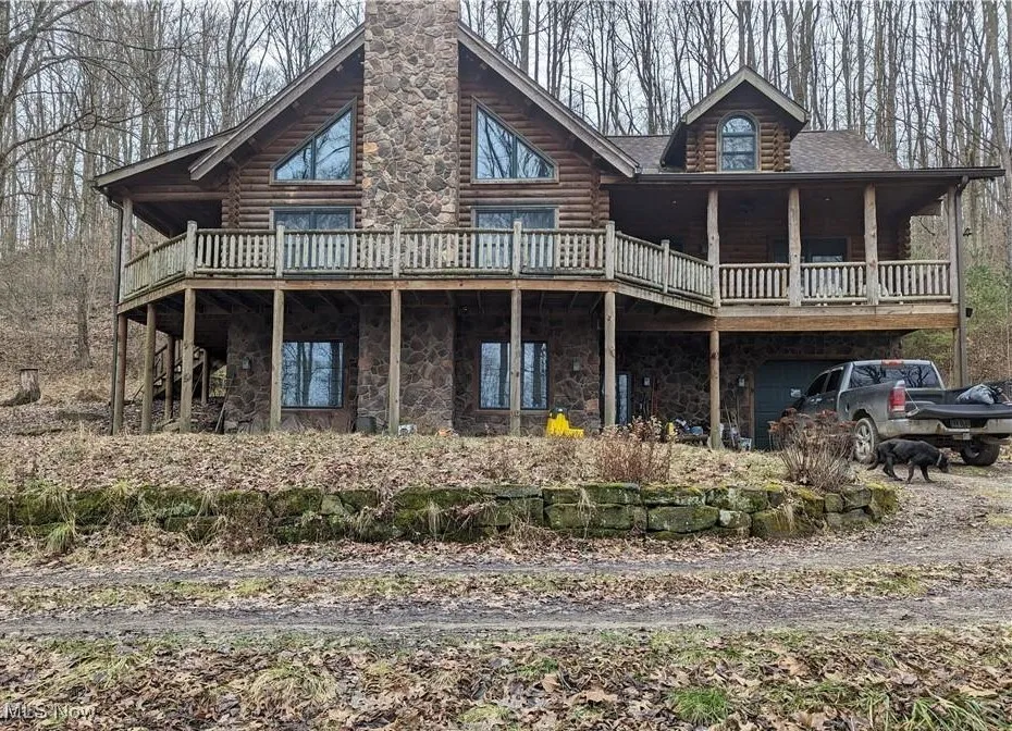 Front of property with log exterior, a wooden deck, stone siding, and a garage