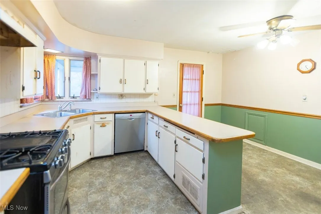 Kitchen with appliances with stainless steel finishes, a peninsula, light countertops, white cabinets, and under cabinet range hood