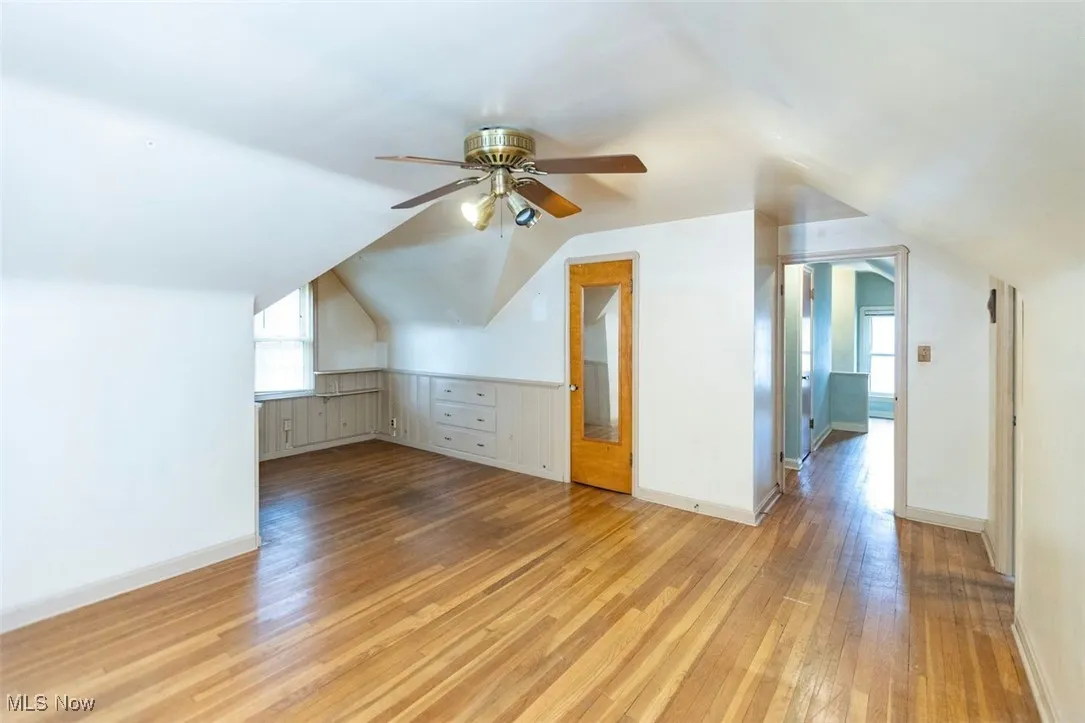 Second floor bedroom with light wood finished floors, vaulted ceiling, and ceiling fan
