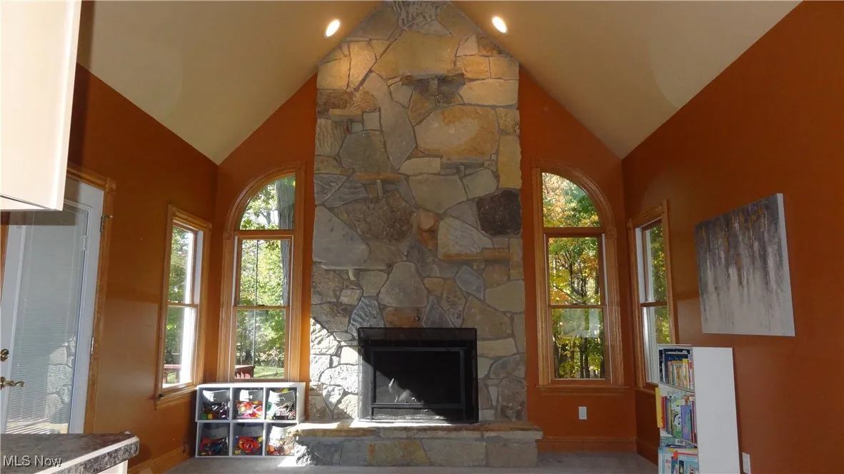 Living area with vaulted ceiling, healthy amount of natural light, and a stone fireplace