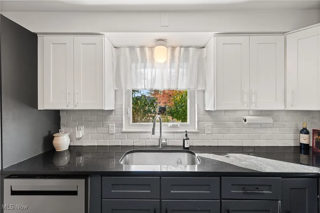 Kitchen with tasteful backsplash, dark stone counters, white cabinets, and dishwasher