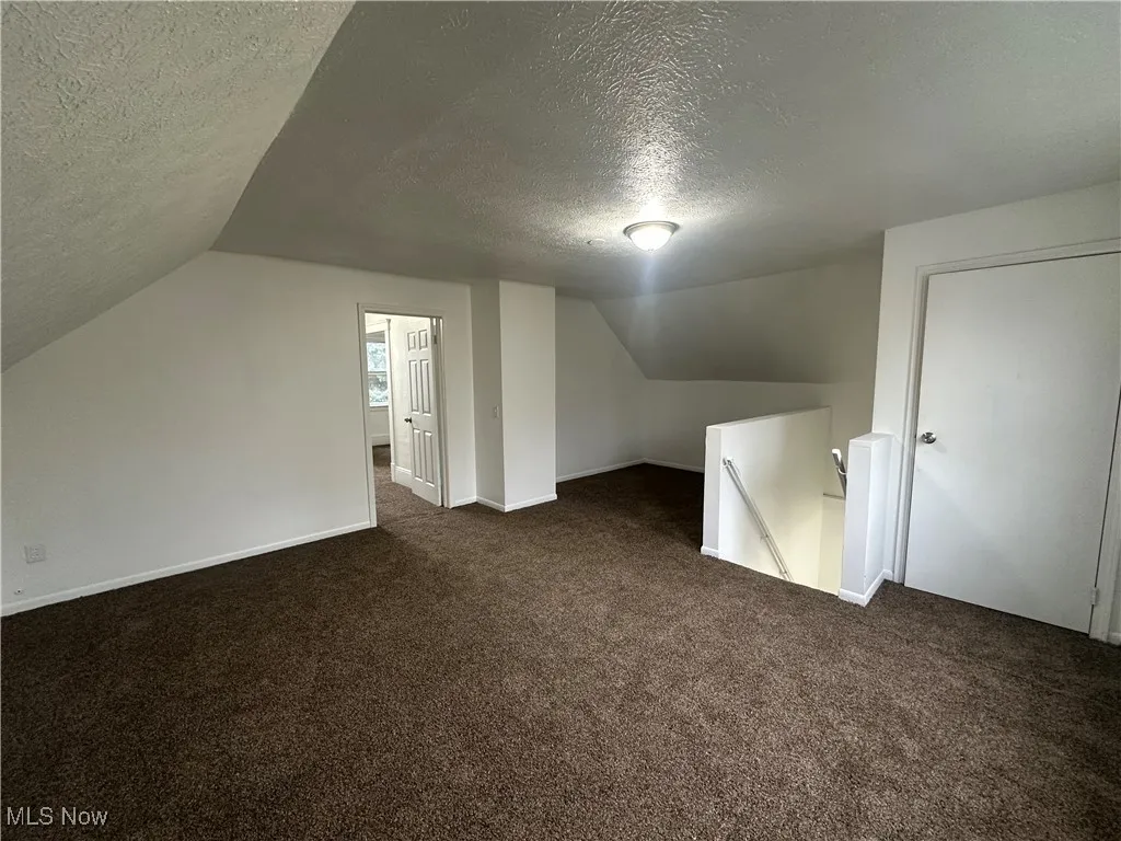 Additional living space with vaulted ceiling, dark carpet, and a textured ceiling