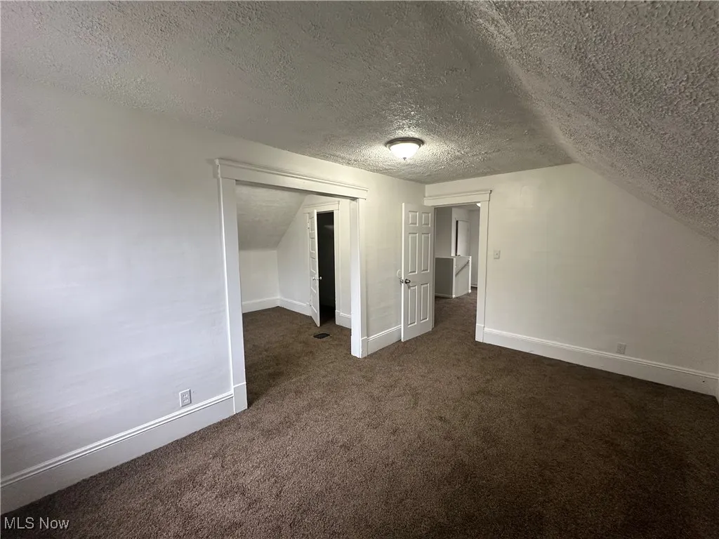 Bonus room with dark carpet, a textured ceiling, and vaulted ceiling