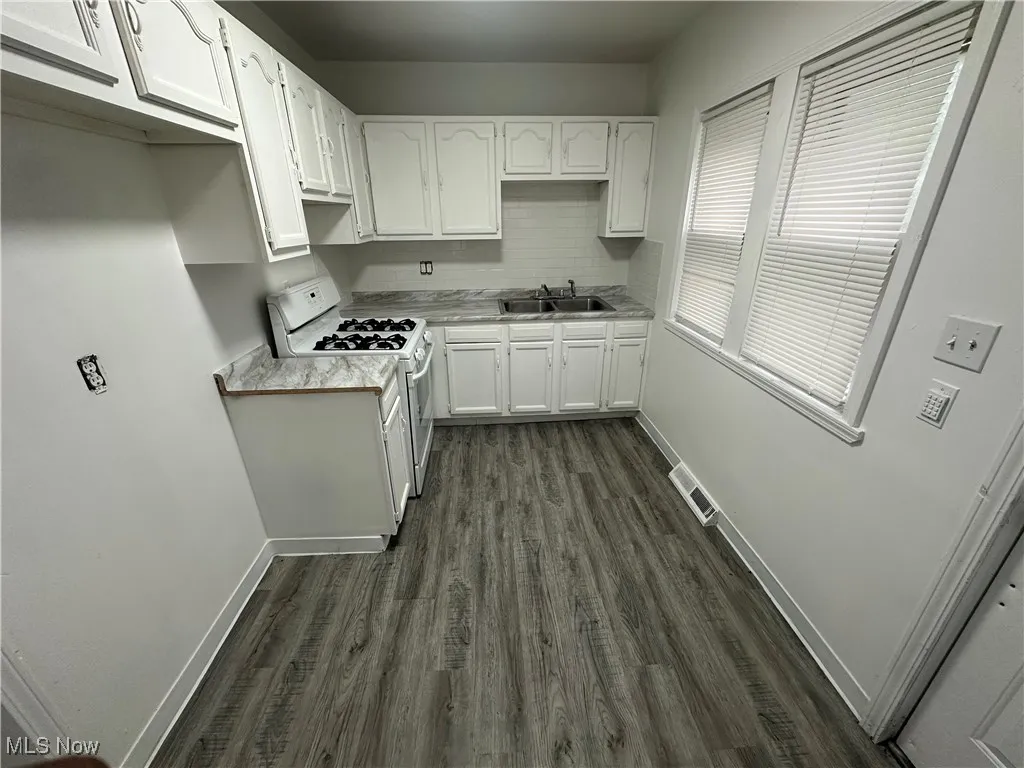 Kitchen with light countertops, white cabinets, dark wood-style floors, white gas stove, and tasteful backsplash