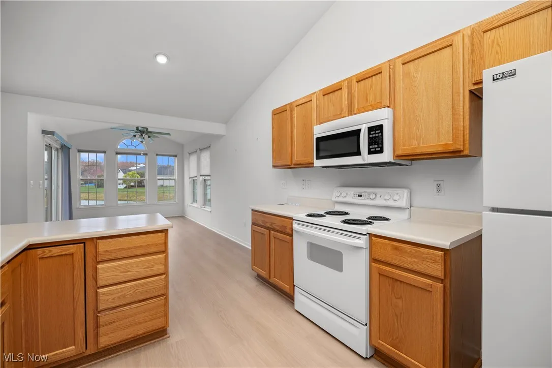 Kitchen featuring white appliances, lofted ceiling, light countertops, light wood-type flooring, and a ceiling fan