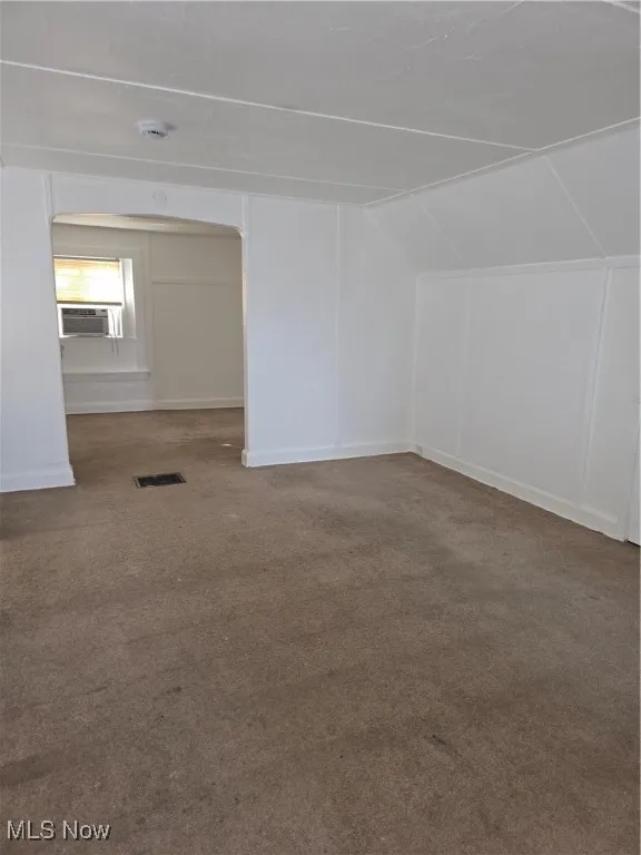 Additional living space featuring carpet, vaulted ceiling, arched walkways, and cooling unit