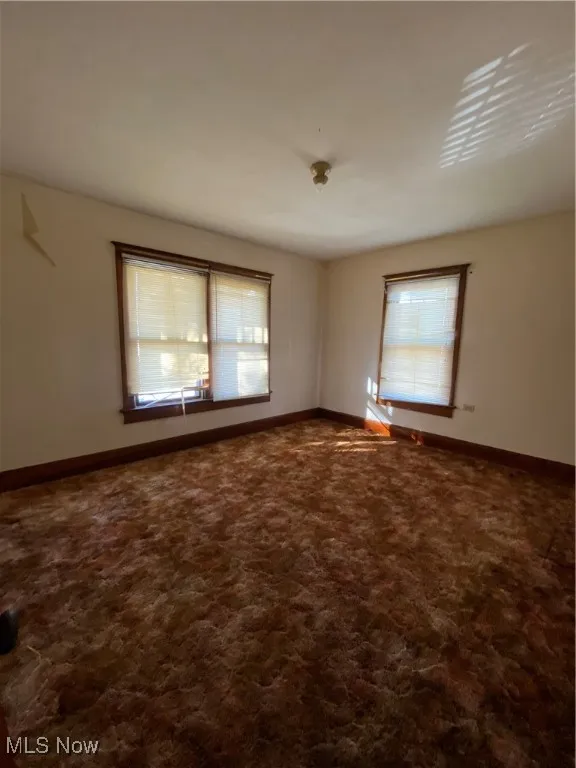 Empty room featuring dark colored carpet and baseboards