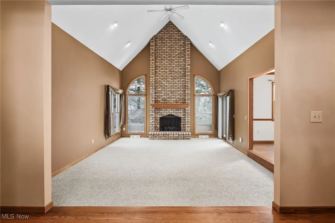 Unfurnished living room with high vaulted ceiling, carpet, a fireplace, a ceiling fan, and wood finished floors