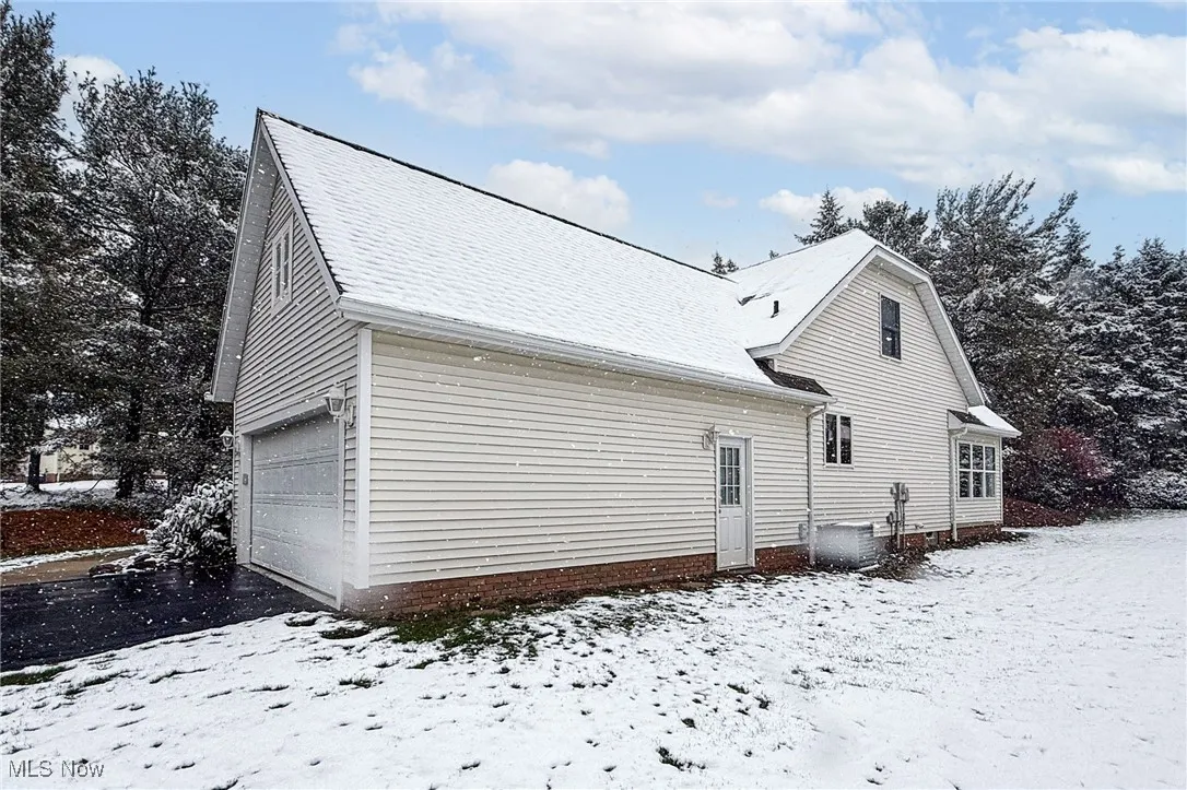 View of snow covered exterior with a garage and a central AC unit
