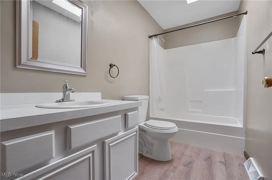 Full bath with light wood lvt floors, vanity, shower / tub combo with curtain, and a skylight