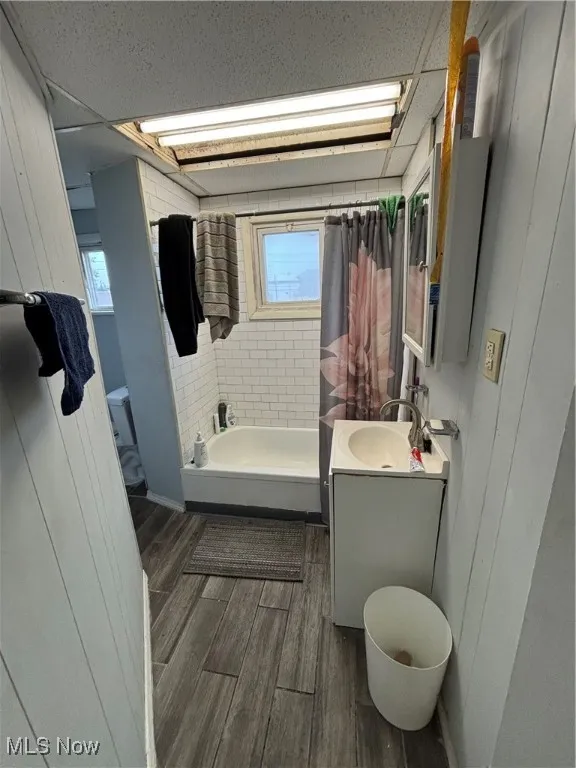 Bathroom with vanity, shower / tub combo with curtain, dark wood finished floors, and wood walls