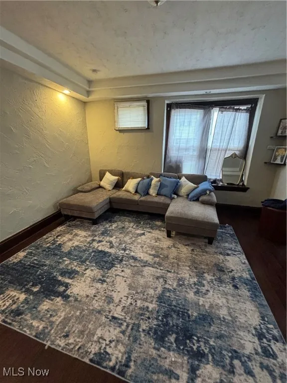 Living area with a textured wall, dark wood-type flooring, and a textured ceiling