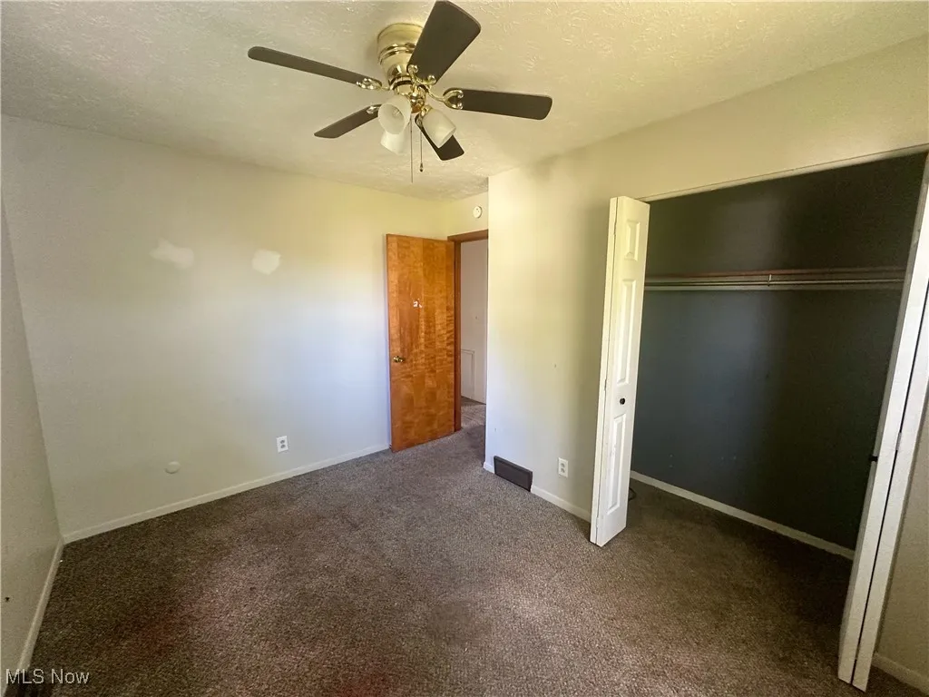 Unfurnished bedroom with a textured ceiling, dark carpet, a closet, and a ceiling fan
