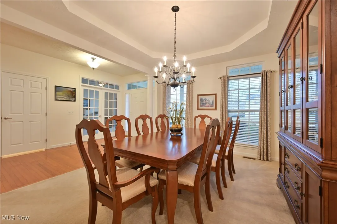 Dining space with french doors, a tray ceiling, a chandelier, light colored carpet, and light wood finished floors