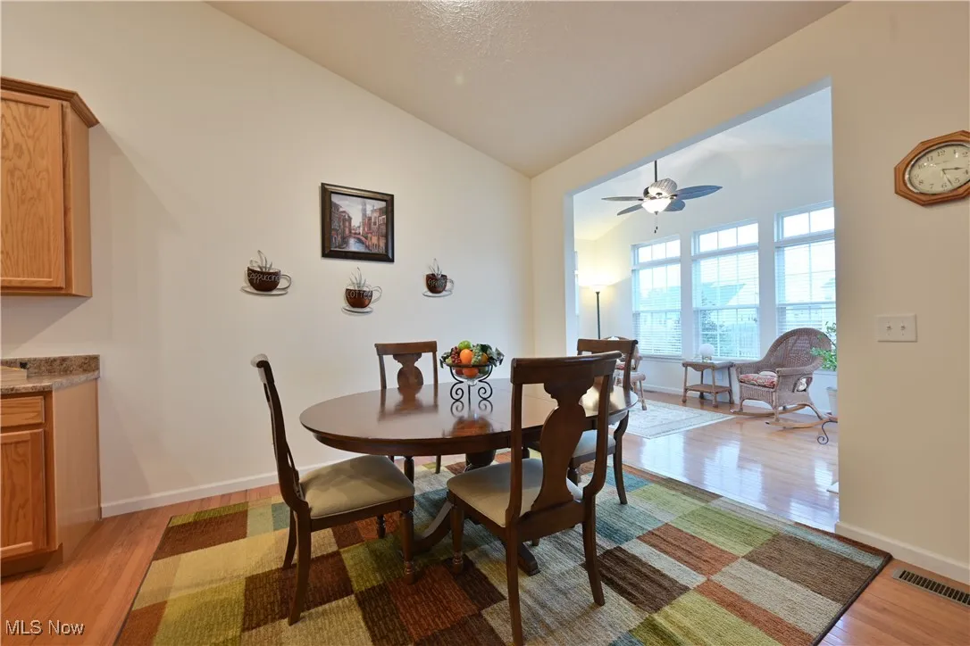 Dining room with light wood-style floors, vaulted ceiling, and a ceiling fan