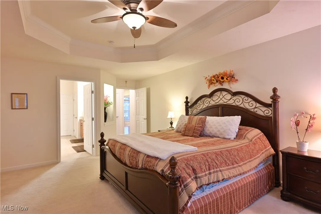 Bedroom with a raised ceiling, crown molding, light carpet, a ceiling fan, and ensuite bathroom