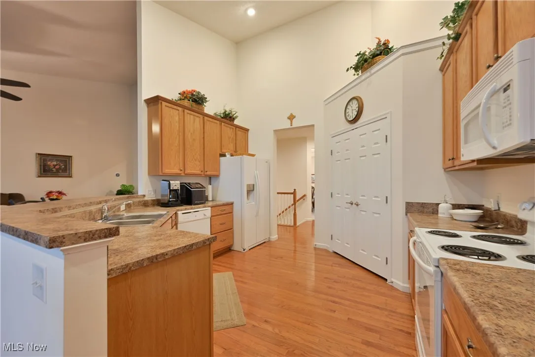 Kitchen featuring white appliances, light wood-style flooring, a peninsula, a high ceiling, and brown cabinets
