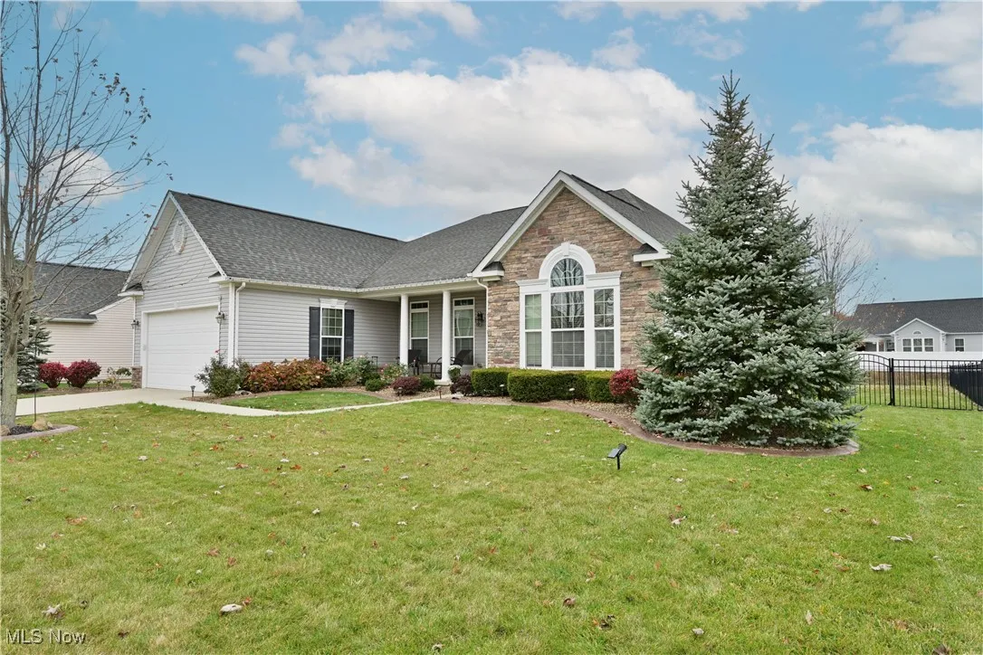 Ranch-style home featuring stone siding, covered porch, roof with shingles, a garage, and driveway