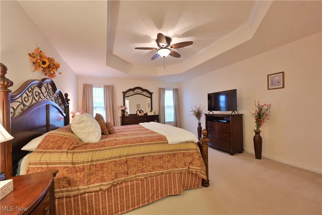 Bedroom with light colored carpet, a raised ceiling, crown molding, and ceiling fan