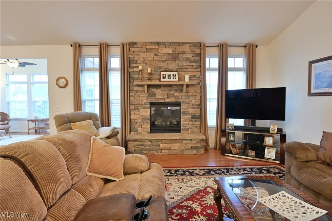 Living room with a stone fireplace, wood finished floors, and ceiling fan