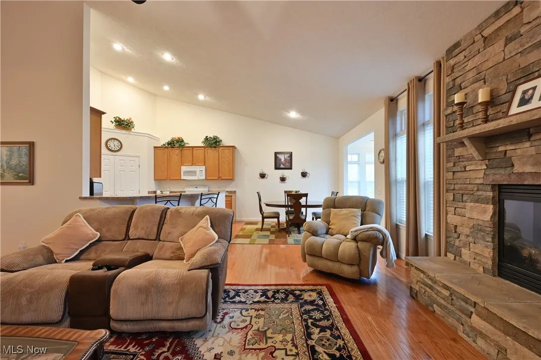 Living room with a fireplace, lofted ceiling, light wood-style flooring, and recessed lighting
