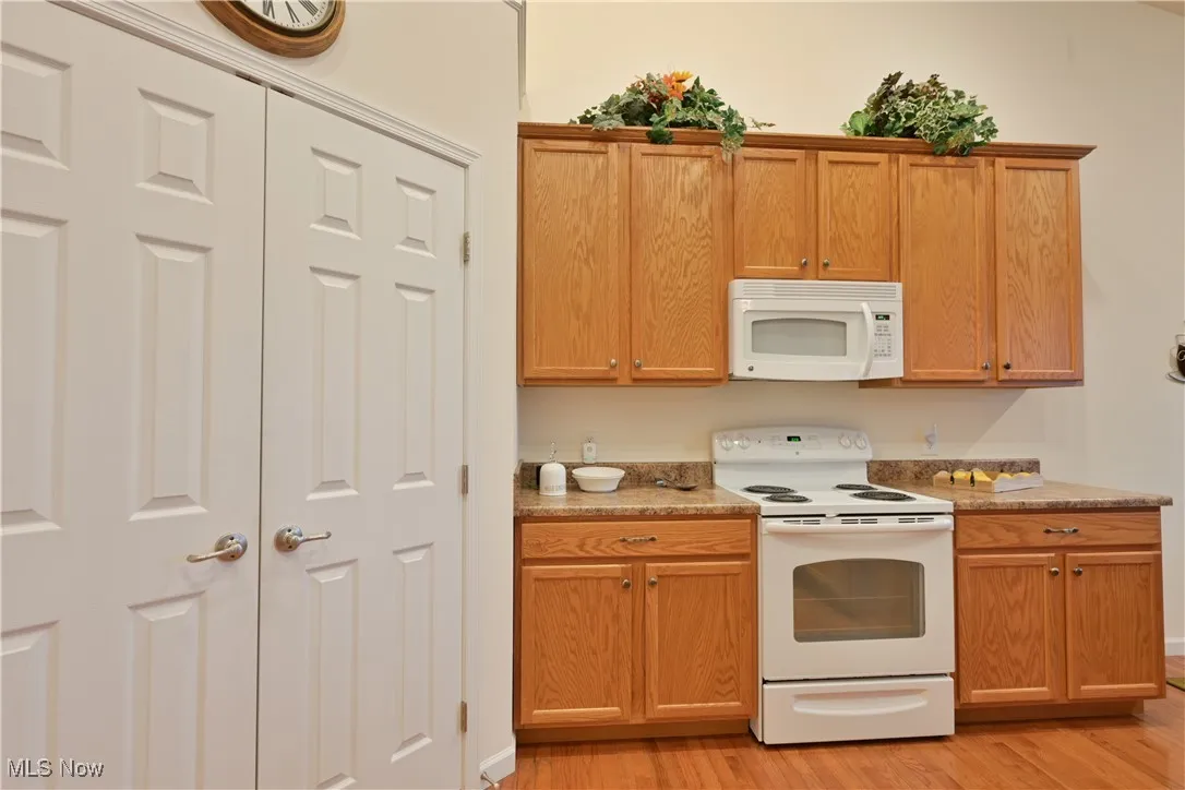 Kitchen with white appliances, light wood-type flooring, light countertops, and brown cabinets