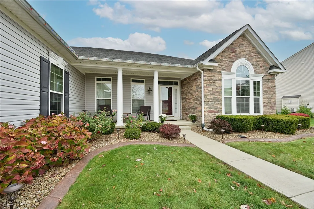 View of front of home featuring a porch, a front lawn, stone siding, and roof with shingles