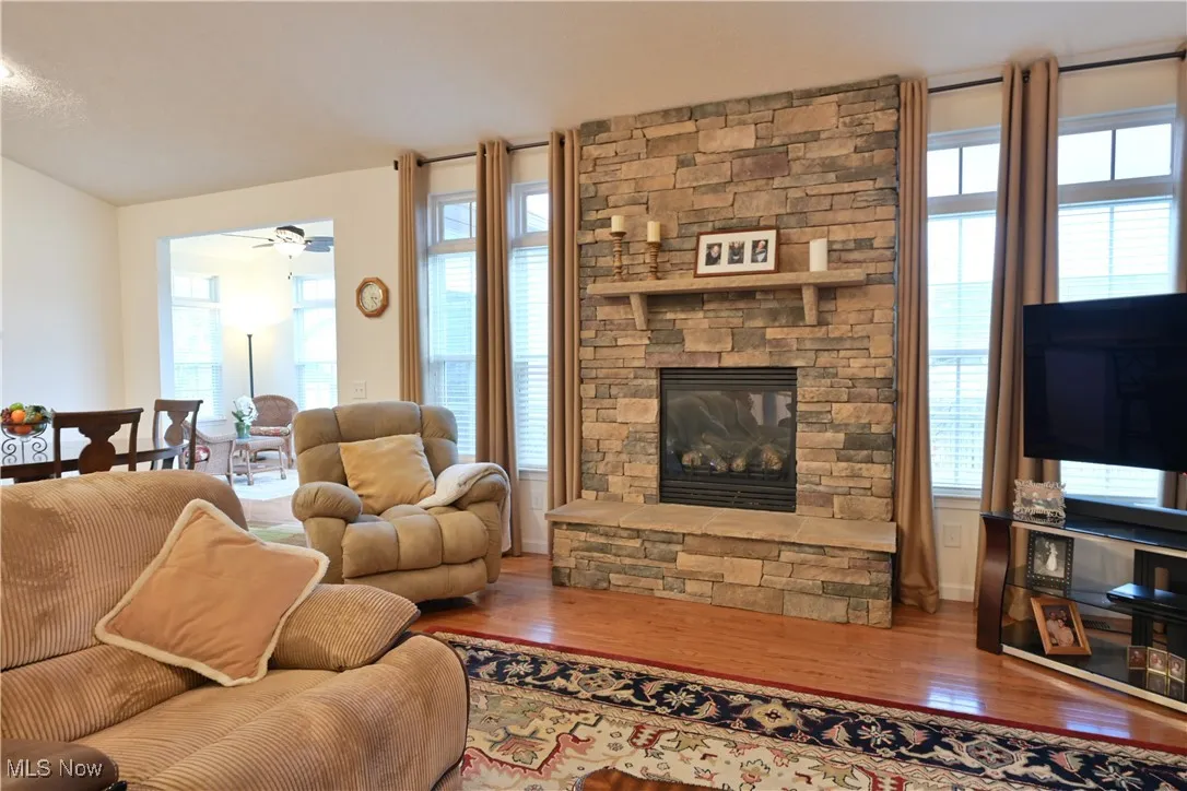 Living area with a stone fireplace, wood finished floors, plenty of natural light, and ceiling fan
