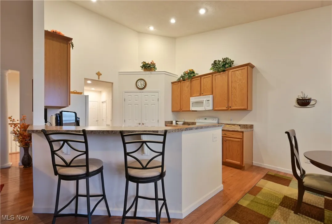 Kitchen with a kitchen breakfast bar, brown cabinets, recessed lighting, light wood-type flooring, and a high ceiling