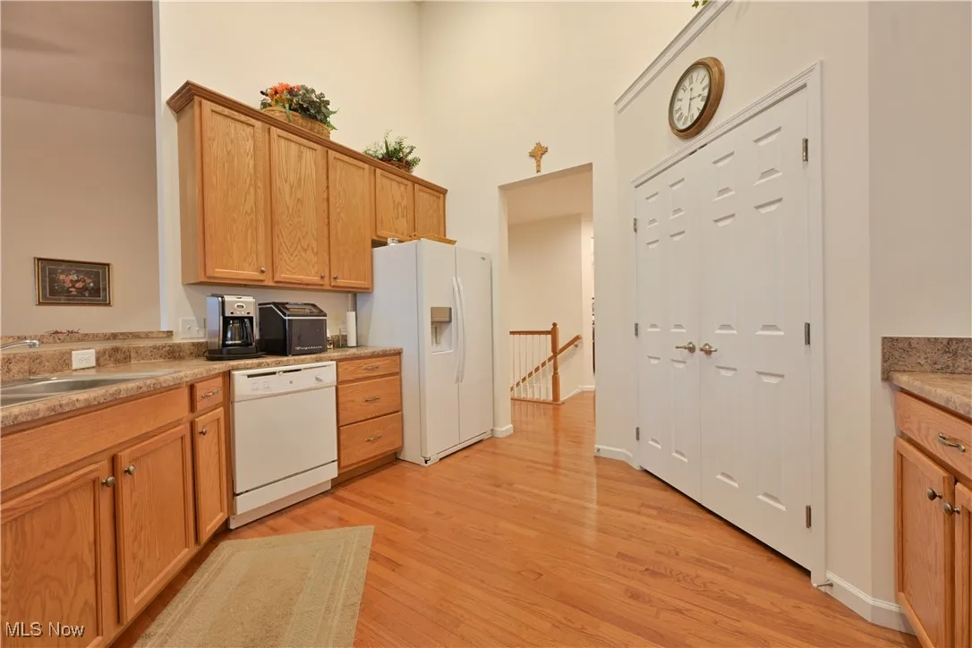 Kitchen with white appliances, light wood-style floors, light countertops, brown cabinetry, and a towering ceiling