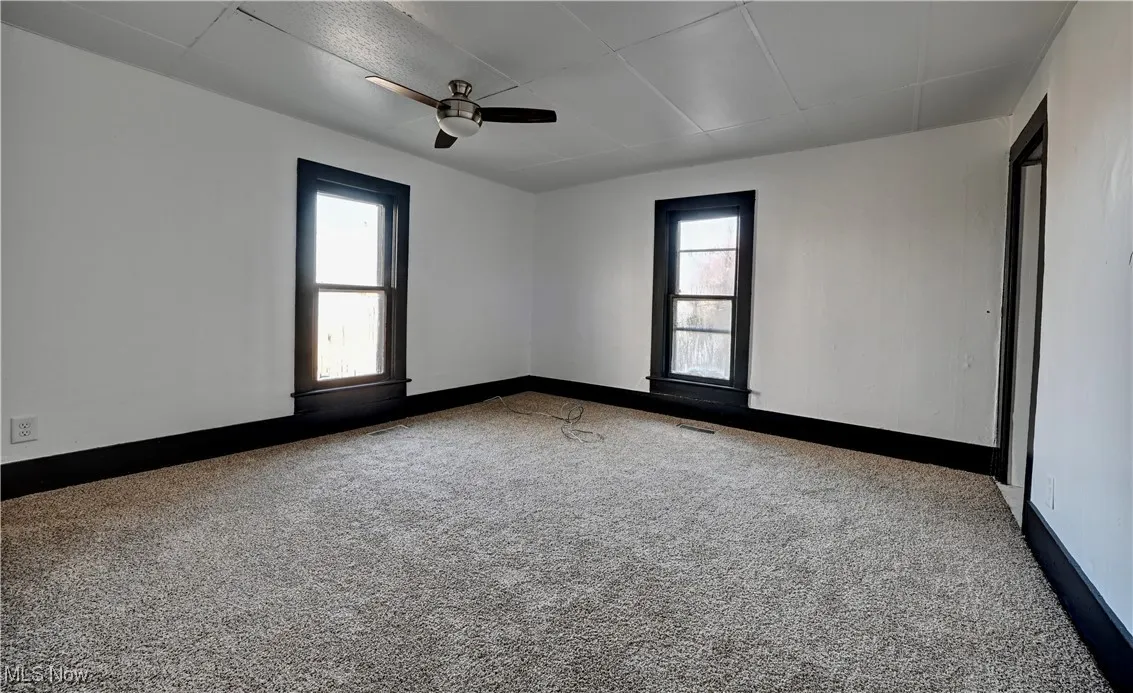 Carpeted empty room with healthy amount of natural light and a ceiling fan