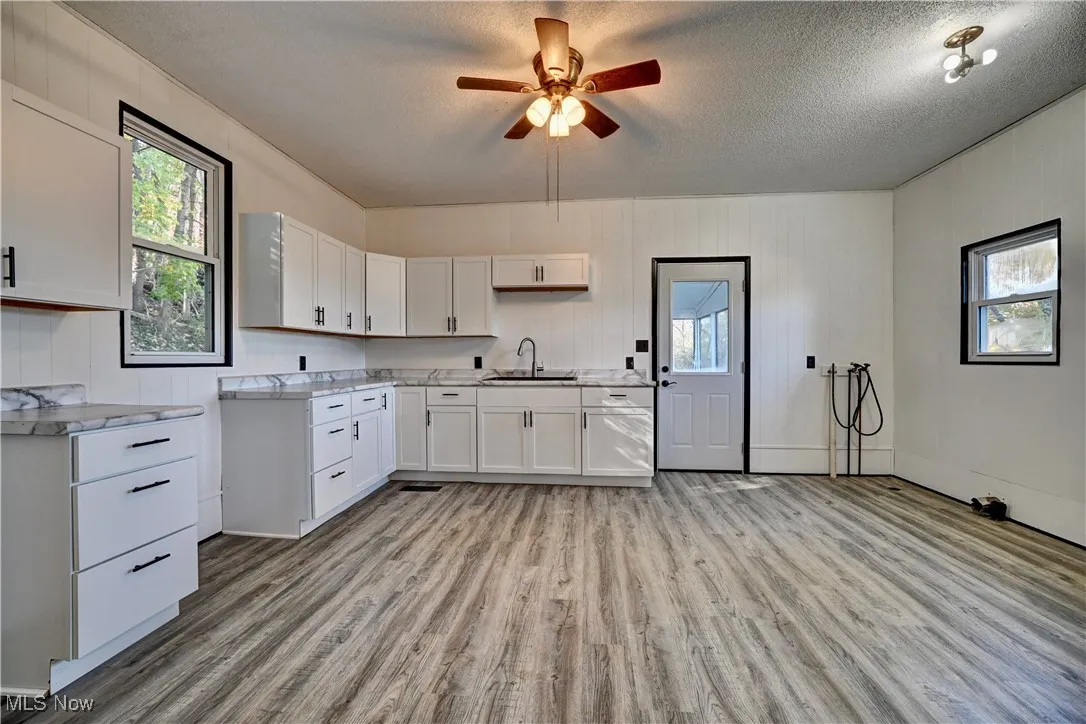 Kitchen with light wood-style flooring, white cabinets, light countertops, ceiling fan, and a textured ceiling