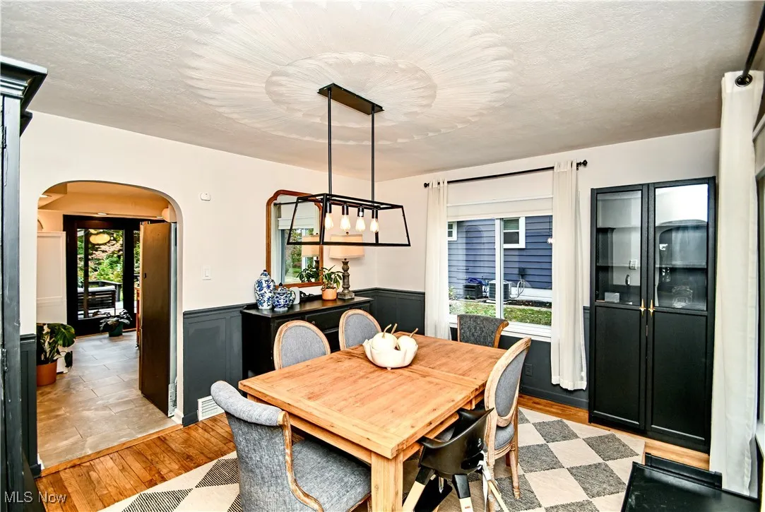 Dining space featuring light wood-type flooring, arched walkways, a wainscoted wall, and a textured ceiling