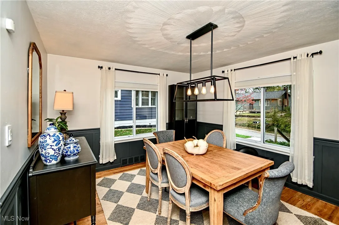 Dining space with wainscoting, wood finished floors, a decorative wall, and a textured ceiling