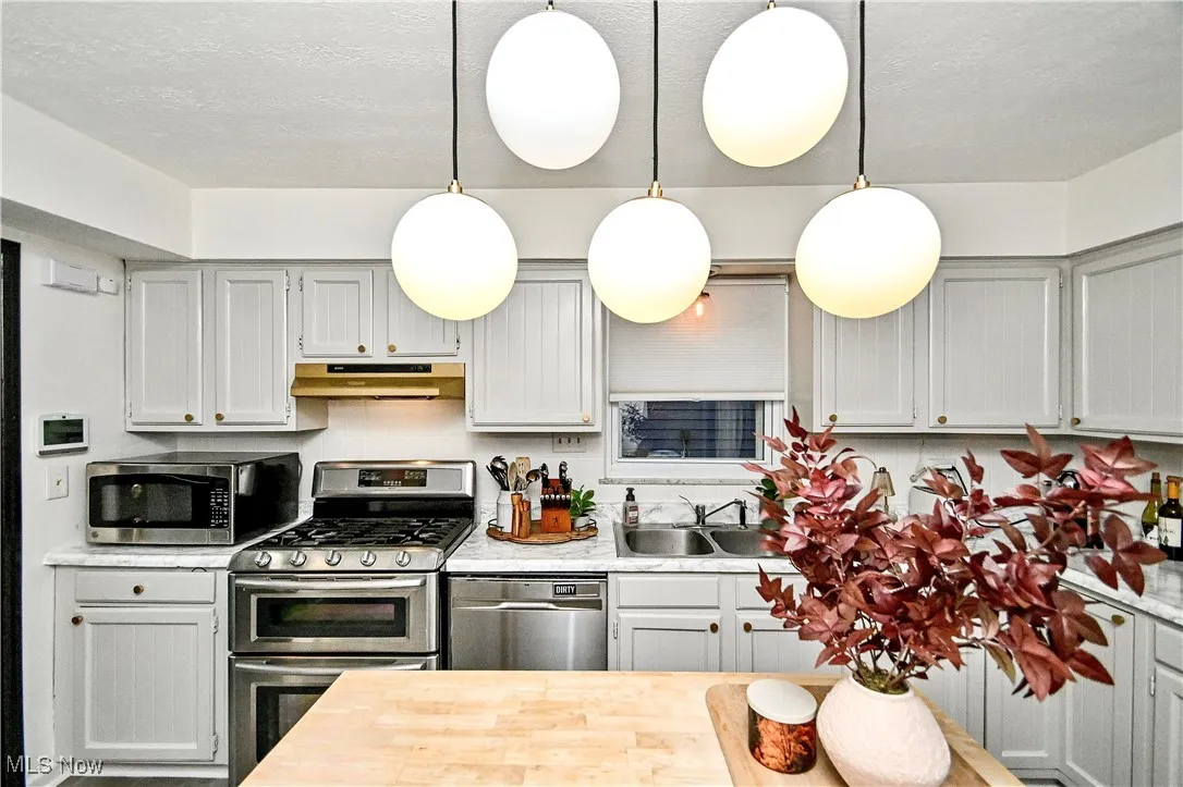Kitchen with appliances with stainless steel finishes, butcher block counters, a textured ceiling, pendant lighting, and gray cabinetry