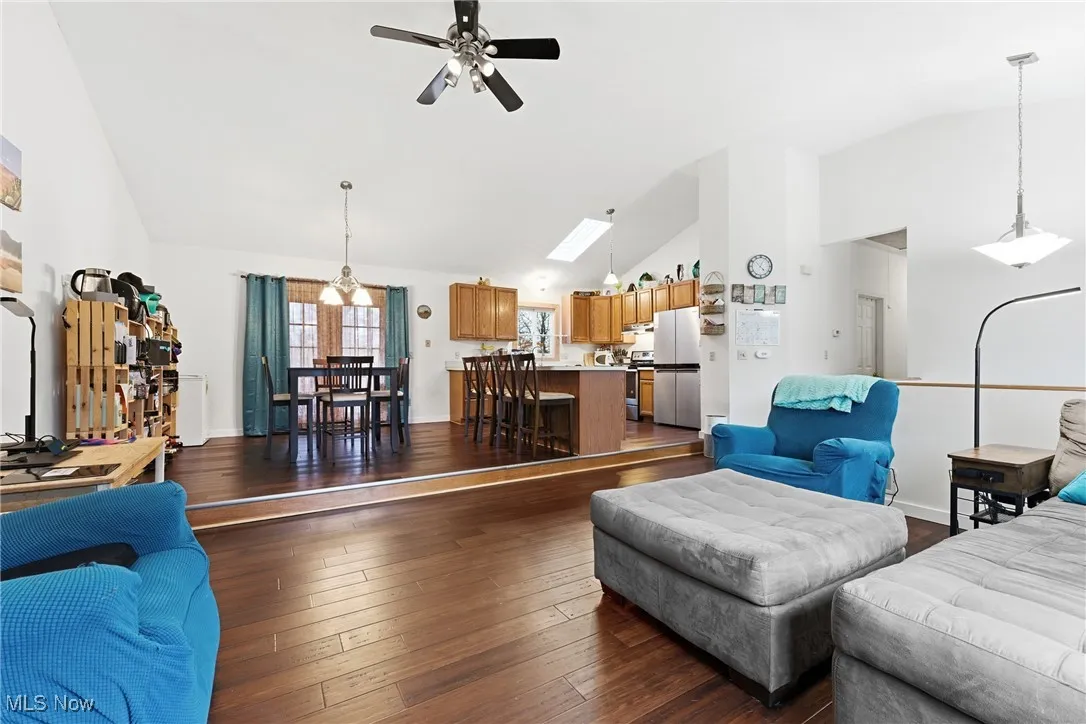 Living area with dark wood-style floors, a ceiling fan, high vaulted ceiling, and a skylight