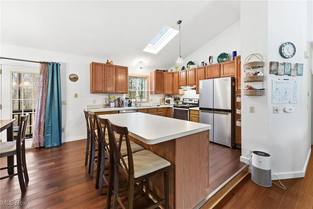 Kitchen with a skylight, appliances with stainless steel finishes, brown cabinets, a breakfast bar area, and decorative light fixtures