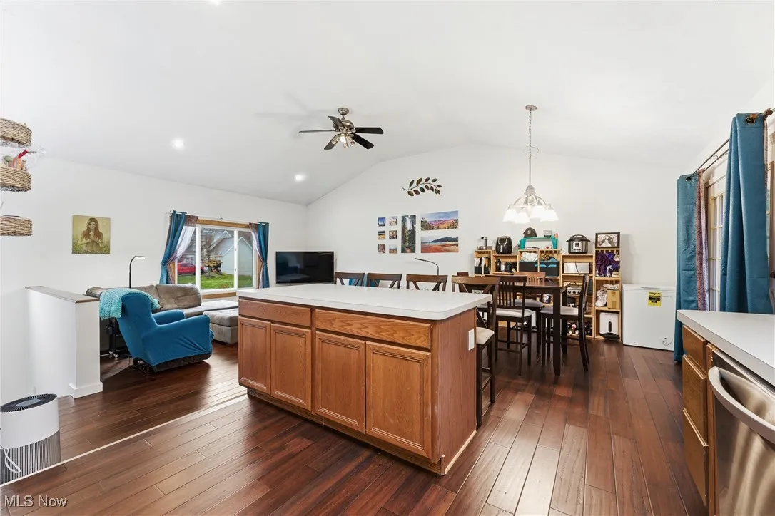 Kitchen featuring brown cabinetry, decorative light fixtures, vaulted ceiling, light countertops, and dishwasher