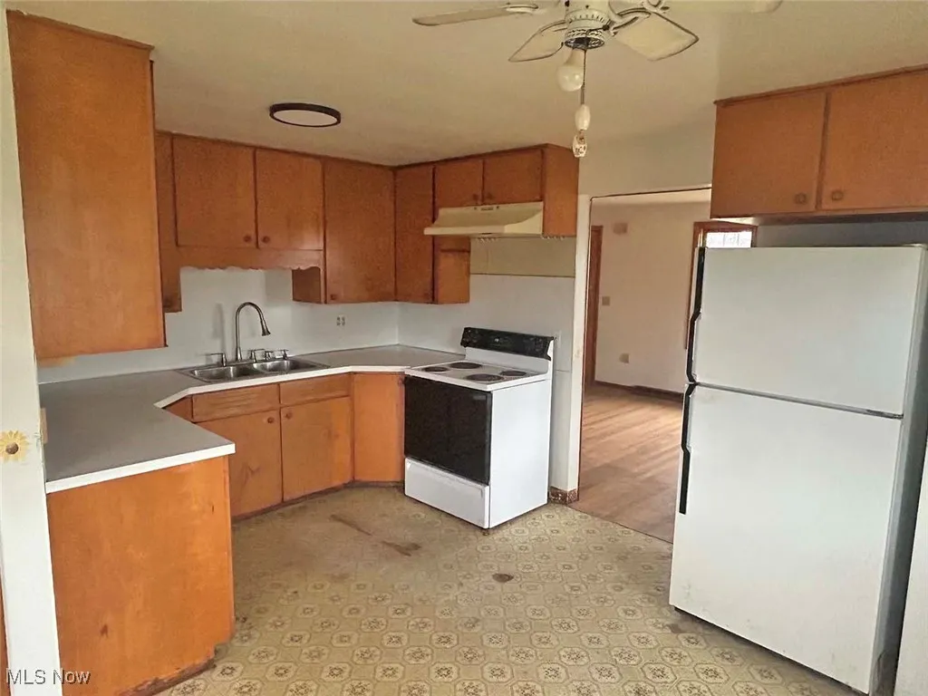 Kitchen with white appliances, brown cabinets, light countertops, and under cabinet range hood