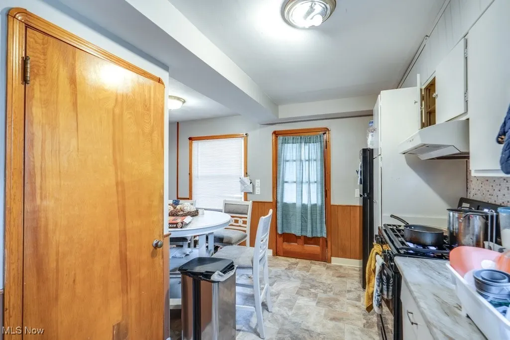 Kitchen featuring a wainscoted wall, wood walls, range hood, stone finish flooring, and light countertops